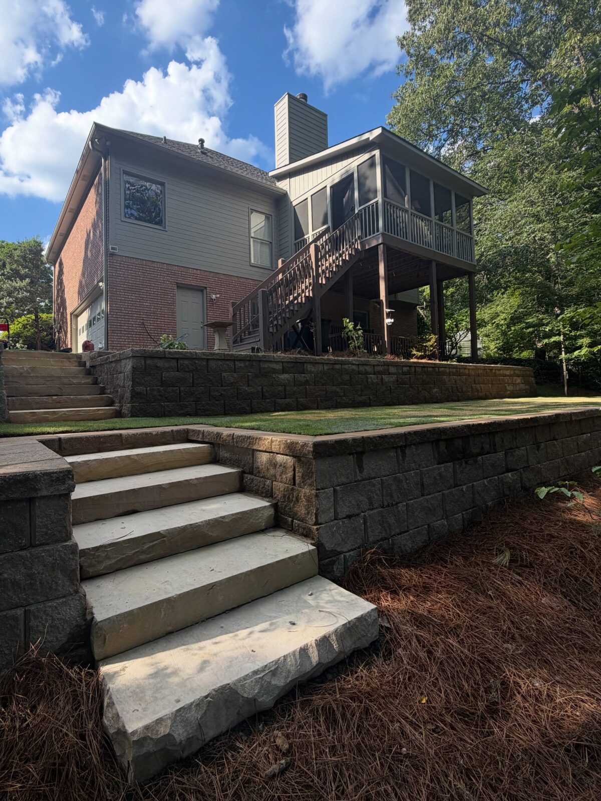 The same backyard finished with a two-tier stacked stone retaining wall, cut stone steps, fresh sod and pine straw.
