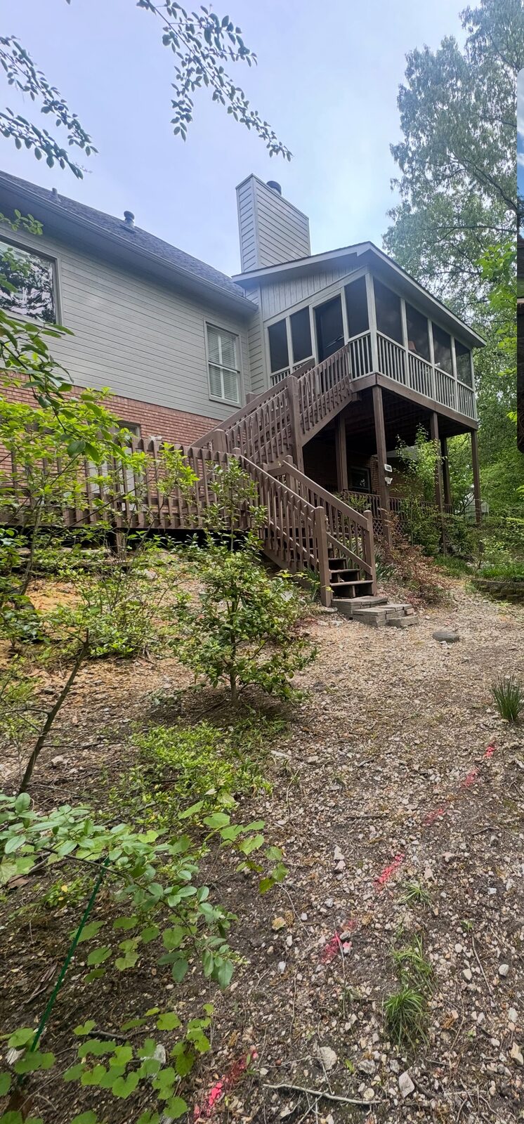 A steep backyard slope of bare dirt, loose rock and weeds beneath a raised screened porch.