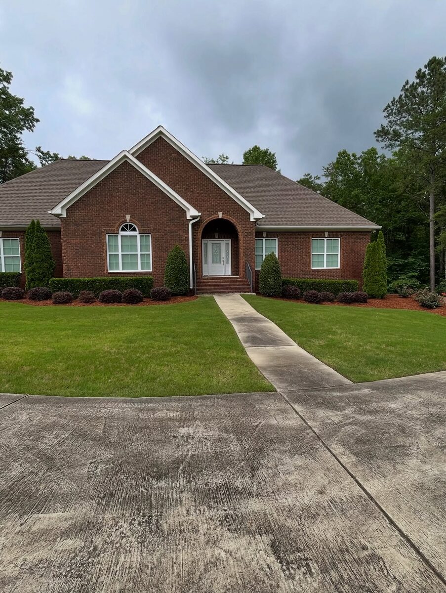 A close-cut lawn and trimmed shrubs in front of a brick ranch house.