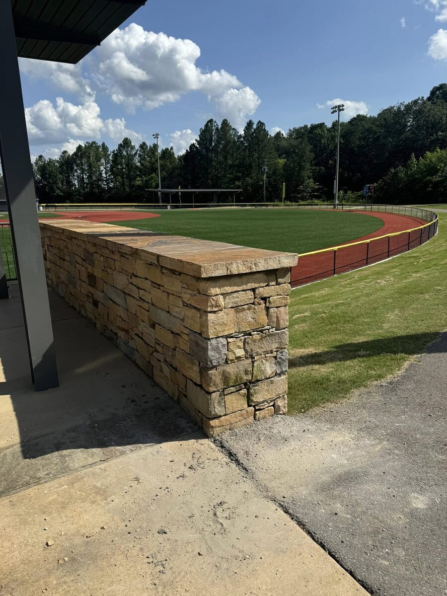 A long stacked stone retaining wall running along the edge of a baseball field.