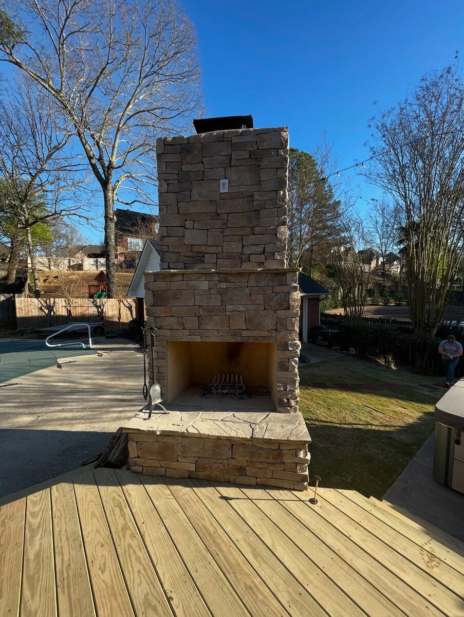 A tall stone outdoor fireplace built at the edge of a wooden deck.